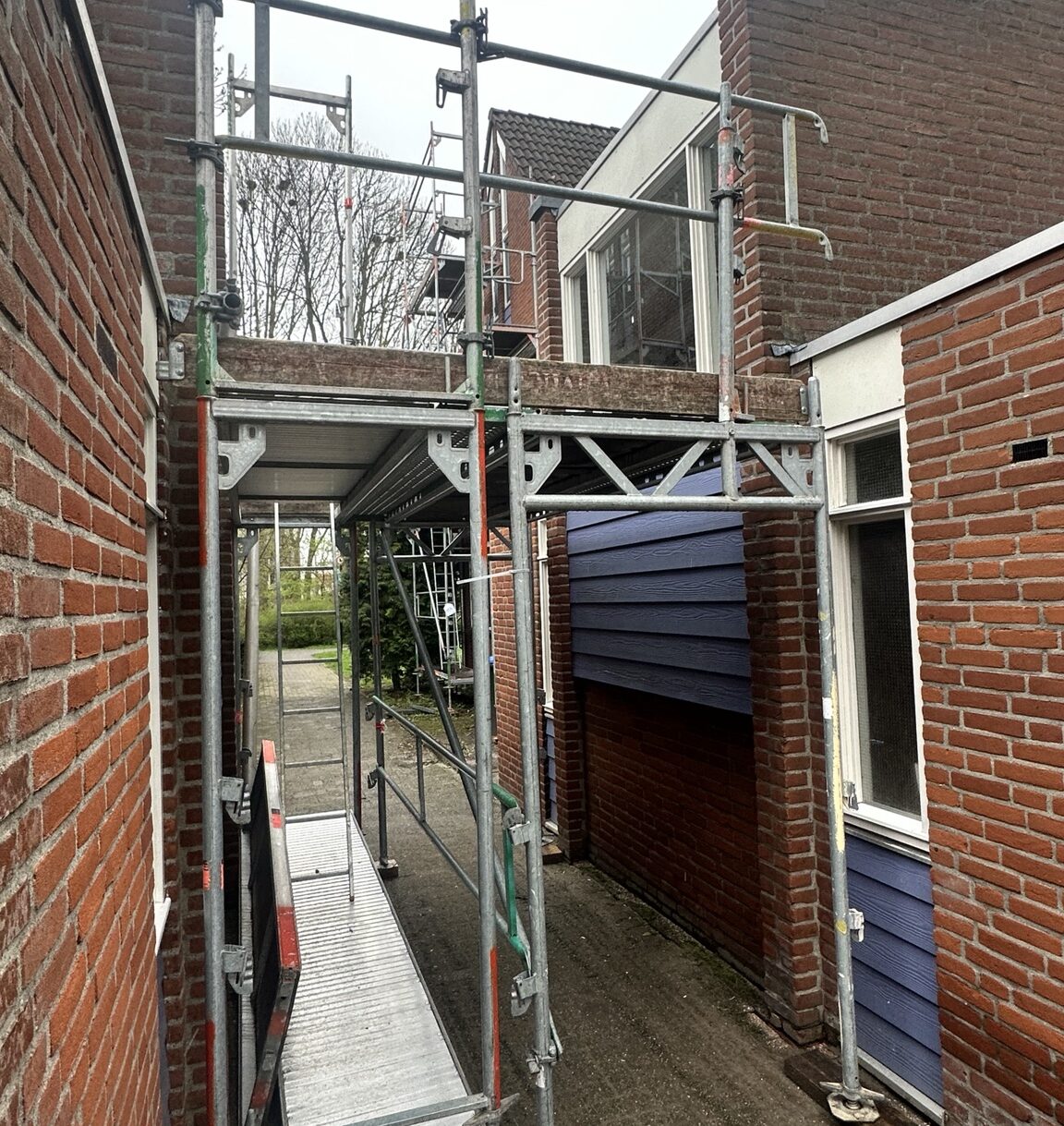 Buitenschilderwerk woningen Lekkerkerk – Voorzijde met doorgang tussen woningen Schilderwerk woningen Lekkerkerk met steigerwerk in doorgang aan voorzijde